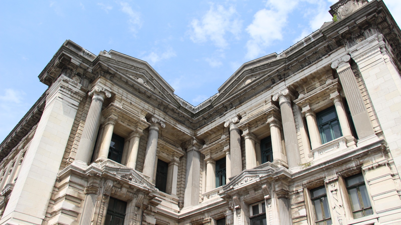 La façade du Palais de Justice de Bruxelles, détail architectural sous un ciel d’été. Photographie réelle, non retouchée. La façade du Palais de Justice de Bruxelles, détail des colonnes et frontons sous un ciel bleu
