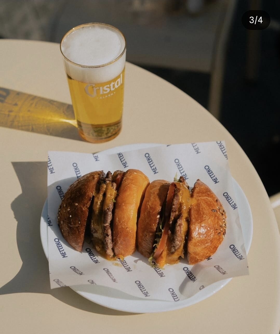 Smash-burger Metteko coupé en deux sur papier griffé, accompagné d’une bière Cristal Alken