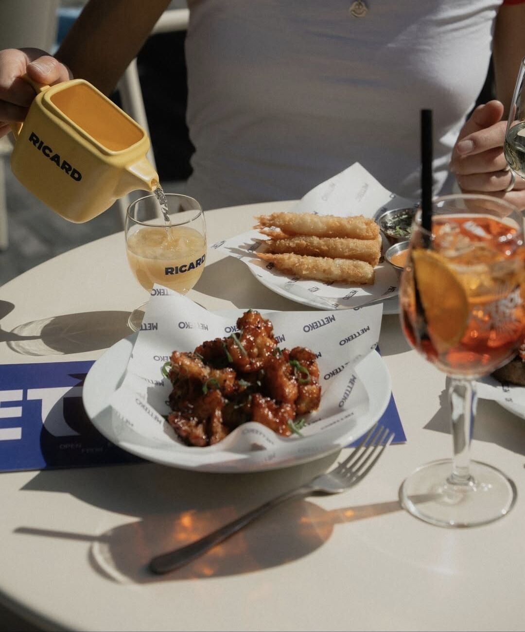 Table en terrasse Metteko : karaage de poulet, tempura de gambas, spritz et carafe Ricard jaune vintage